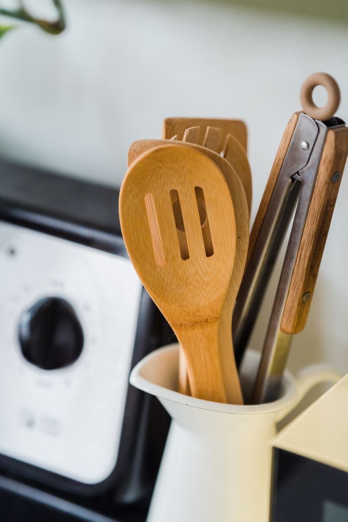 who-we-are Close-up of wooden and metal kitchen utensils in a white container on a kitchen countertop.